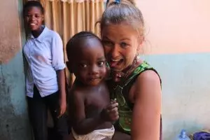Luisa Frick hält ein schwarzes Baby auf dem Arm. Im Hintergrund steht eine schwarze Frau, die lächelt.