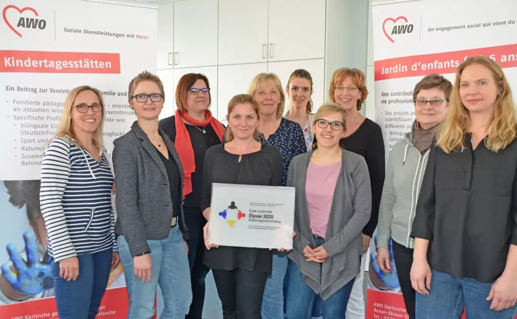 Auf dem Bild zu sehen sind zehn junge Frauen, die im Bereich Kitas der AWO Karlsruhe arbeiten, eine von ihnen hält „Ecoles maternelles / Bilinguale Kindertageseinrichtung – Elysée 2020“ - die Auszeichnung für die bilinguale Arbeit in den Händen. 