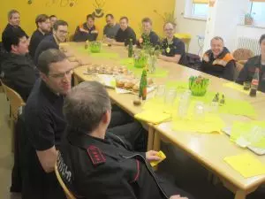 Die Mitglieder der freiwilligen Feuerwehr Grötzingen sitzen an einem gedeckten Tisch und sehen fröhlich aus.
