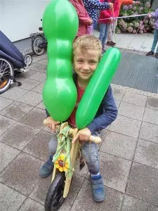 Ein fünfjähriger Junge sitzt auf einem Laufrad an dem zwei grüne Luftballons befestigt sind.
