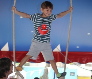 Ein Junge steht auf einer Schaukel in einem Zirkuszelt.