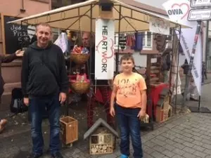 Ein Mann und sein Sohn stehen vor dem Stand des AWO Arbeitsprojektes mit den Handgefertigten Produkten.