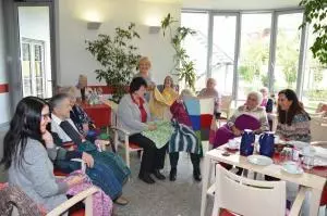 Eine Gruppe von Senioren und ihre Betreuer schauen sich bunte Wolldecken an.