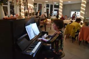 Eine Frau sitzt am Klavier und spielt für ein paar Menschen, die an Tischen sitzen.