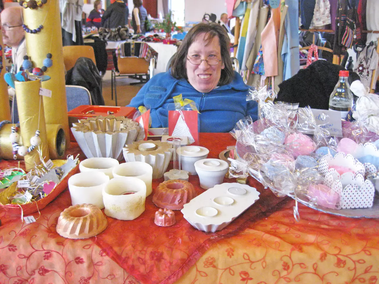 Eine Frau im Rollstuhl sitzt an einem Stand und verkauft handgefertigte Waren.