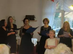 Vier Frauen und ein Kind stehen vor Menschen und singen.