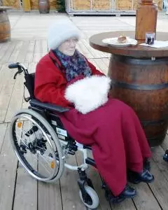 Eine Seniorin sitzt im Rollstuhl an einer Glühweinbude.