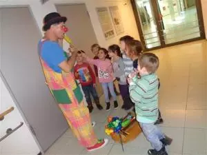 Kinder der AWO Kita les petits amis stehen um einen Clown herum und lachen.