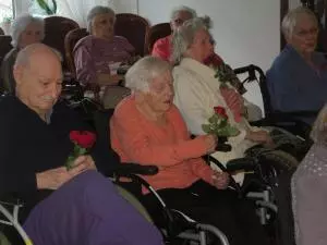 Senior*innen sitzen in Rollstühlen und halten Rosen in den Händen.