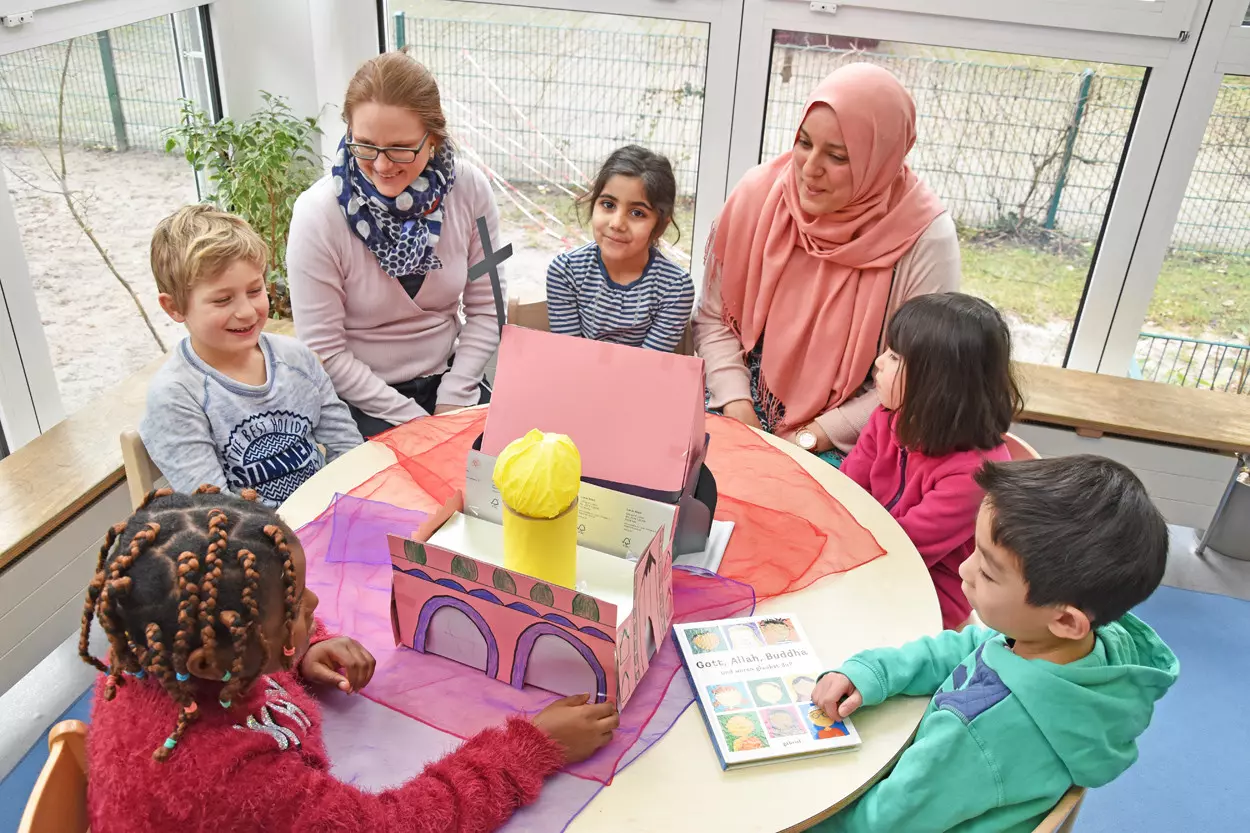 Kinder sitzen mit zwei erwachsenen Frauen an einem Tisch und unterhalten sich.