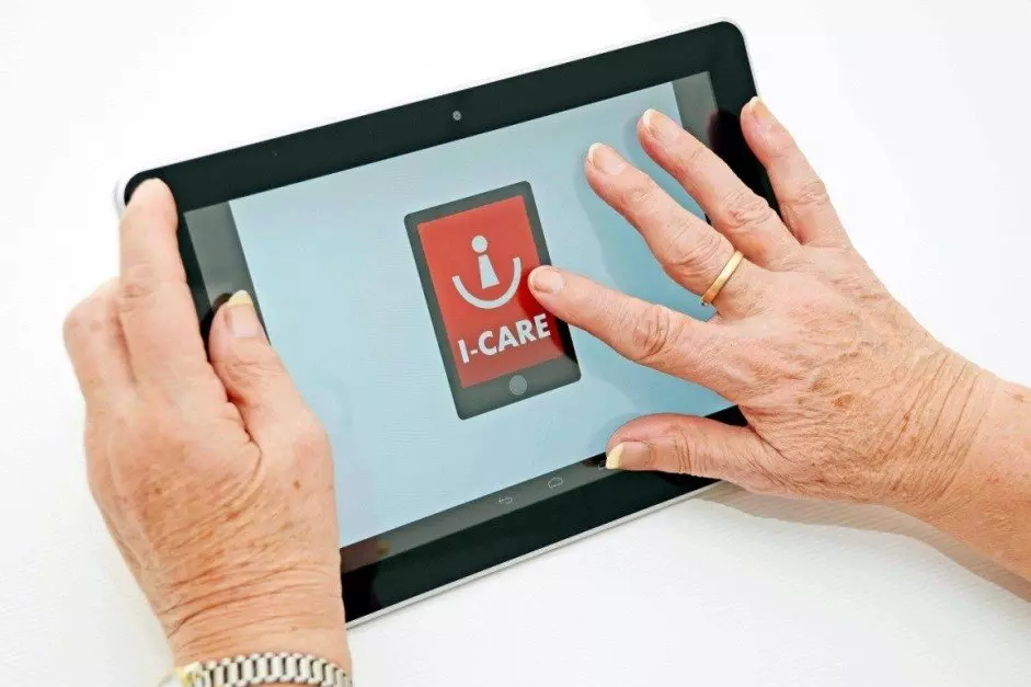 Eine Seniorin streicht über ein Tablet mit einem I-CARE Logo.
