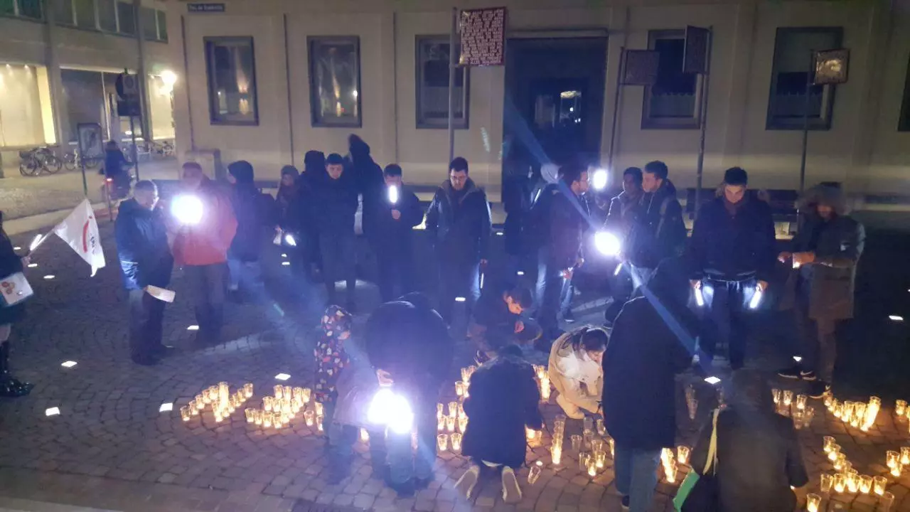 Menschen stehen in der Dämmerung und zünden Teelichter an.