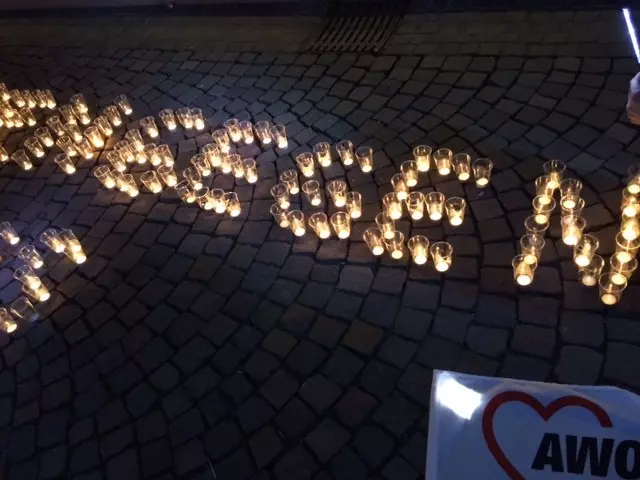 Teelichter stehen auf dem Boden, danben liegt eine Fahne mit einem AWO Herz.