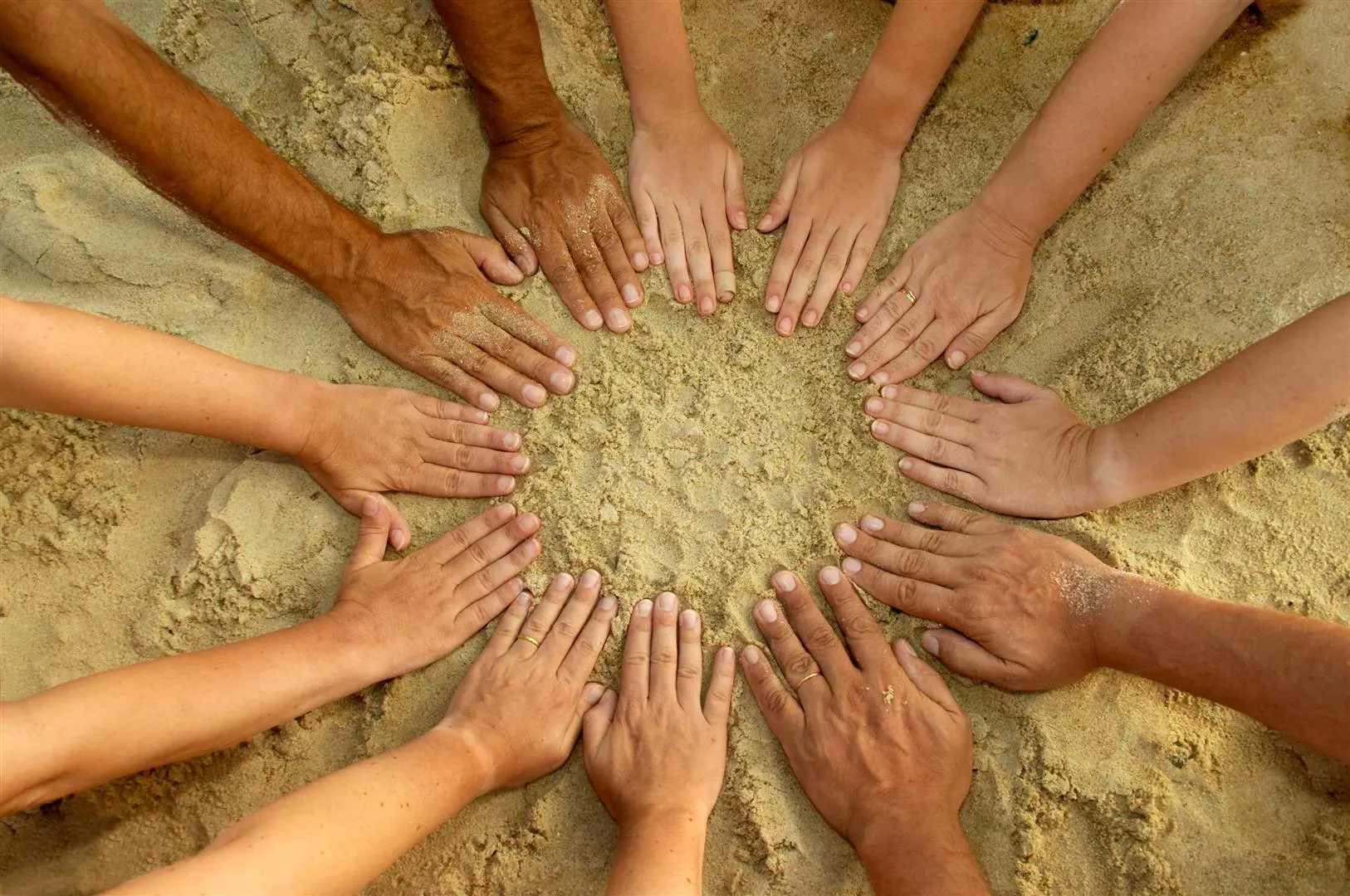 Hände mit verschiedenen Hauttönen bilden einen Kreis im Sand.