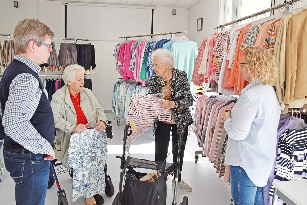 Zwei Seniorinnen stehen vor Kleiderständern und schauen sich Bekleidung an.