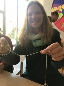 Eine blonde Frau hält einen Faden mit Papier zwischen beiden Zeigefingern und Daumen.