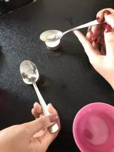 Zwei Hände halten Löffel mit einer Flüssigkeit fest, die über einem Teelicht erwärmt wird.