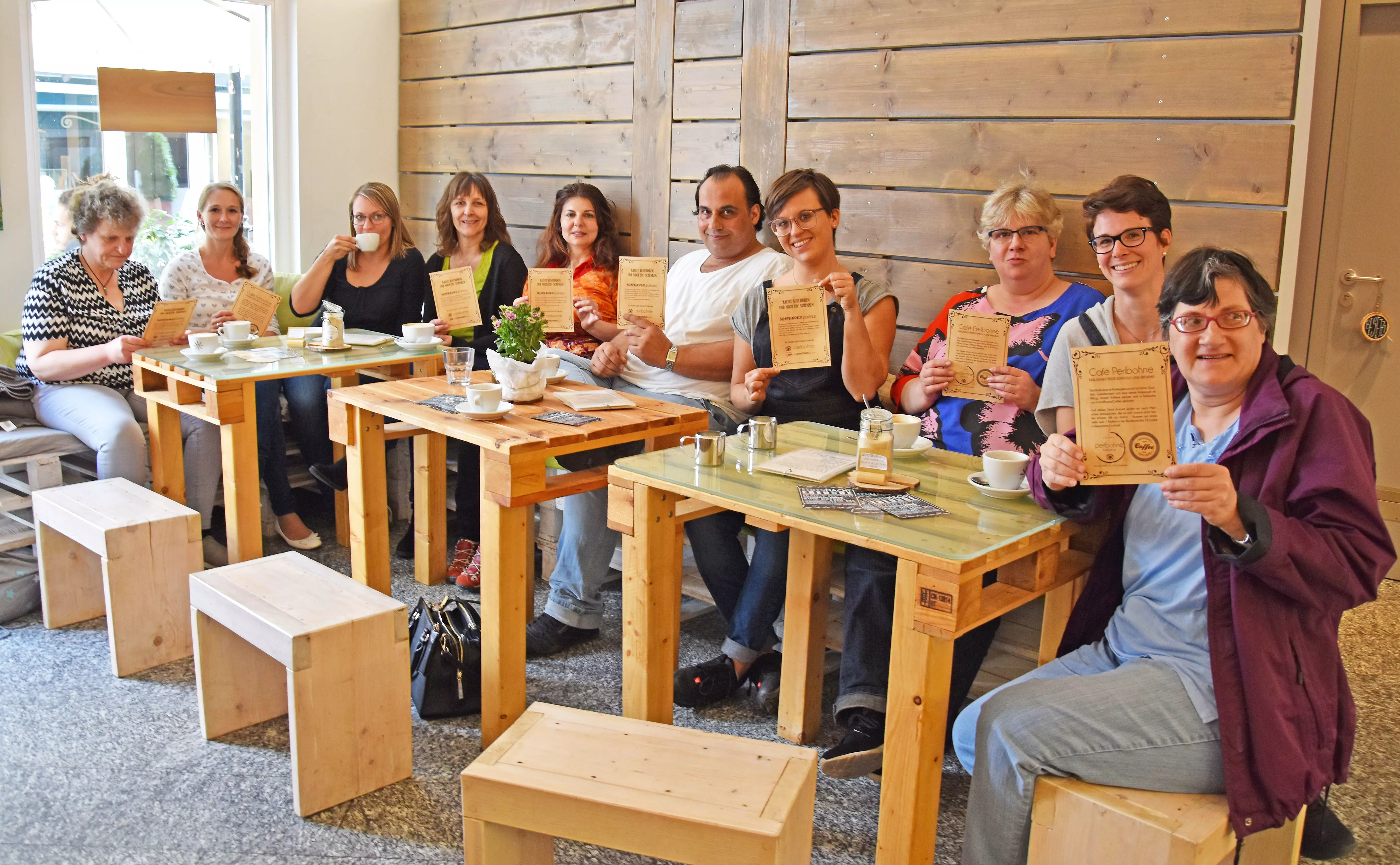 Menschen sitzen an einem Tisch halten Zettel in die Luft und trinken Kaffee.