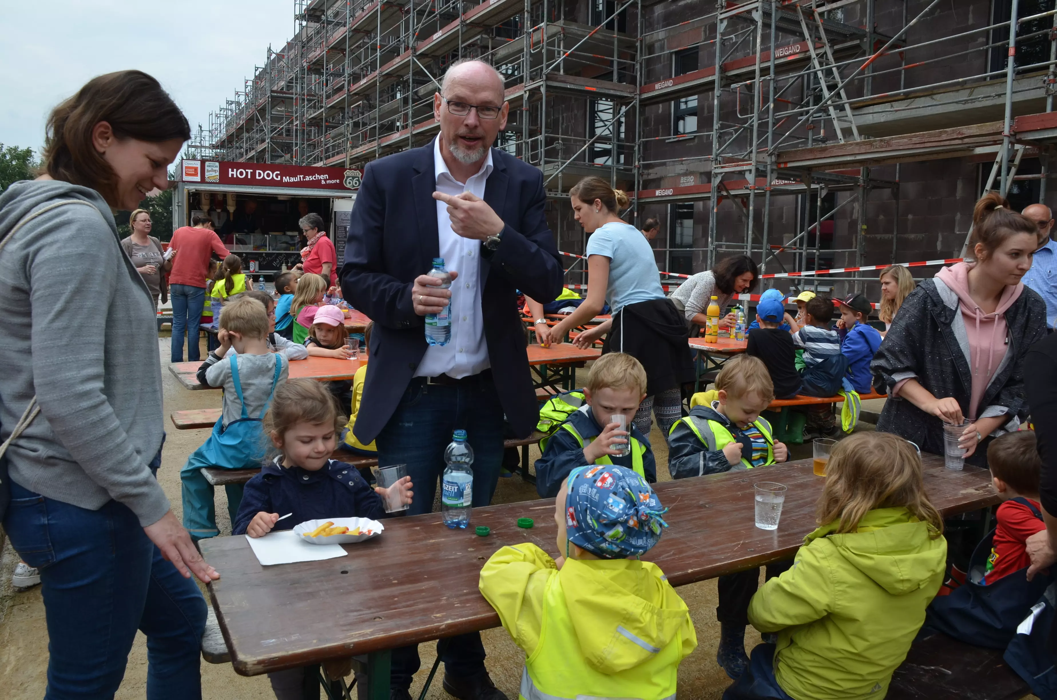 Kinder sitzen vor einem Foodtruck auf Bierbänken und essen etwas.