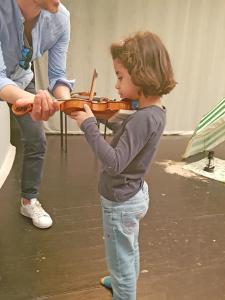 Ein kleins Mädchen hält eine Geige fest, ein Erwachsener hilft ihr dabei.