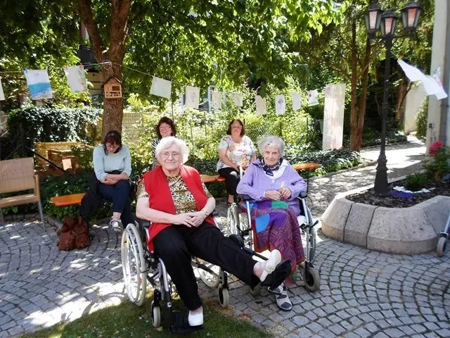 Menschen sitzen in Rollstühlen in einem Hof.