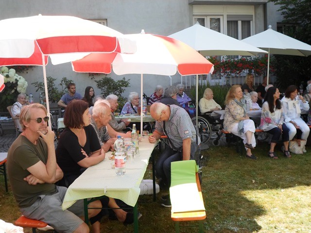 Menschen sitzen auf Bierbänken an einem Tisch unter Sonnenschirmen.