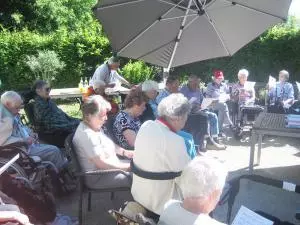 Senioren sitzen im Garten unter einem Sonnenschirm.