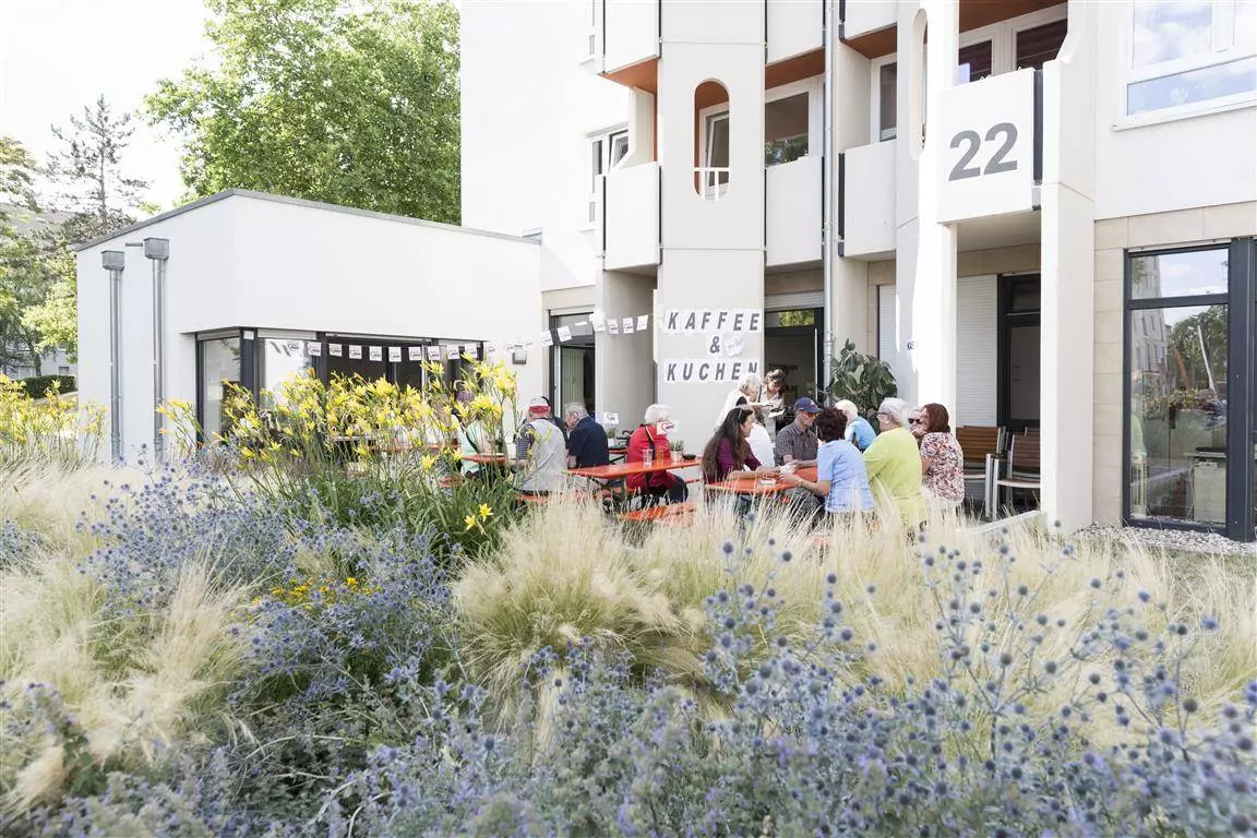 Menschen sitzen auf einer Terrasse auf Bänken an Tischen.