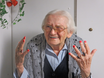 Eine ältere Dame zeigt ihre rot lakierten Nägel.