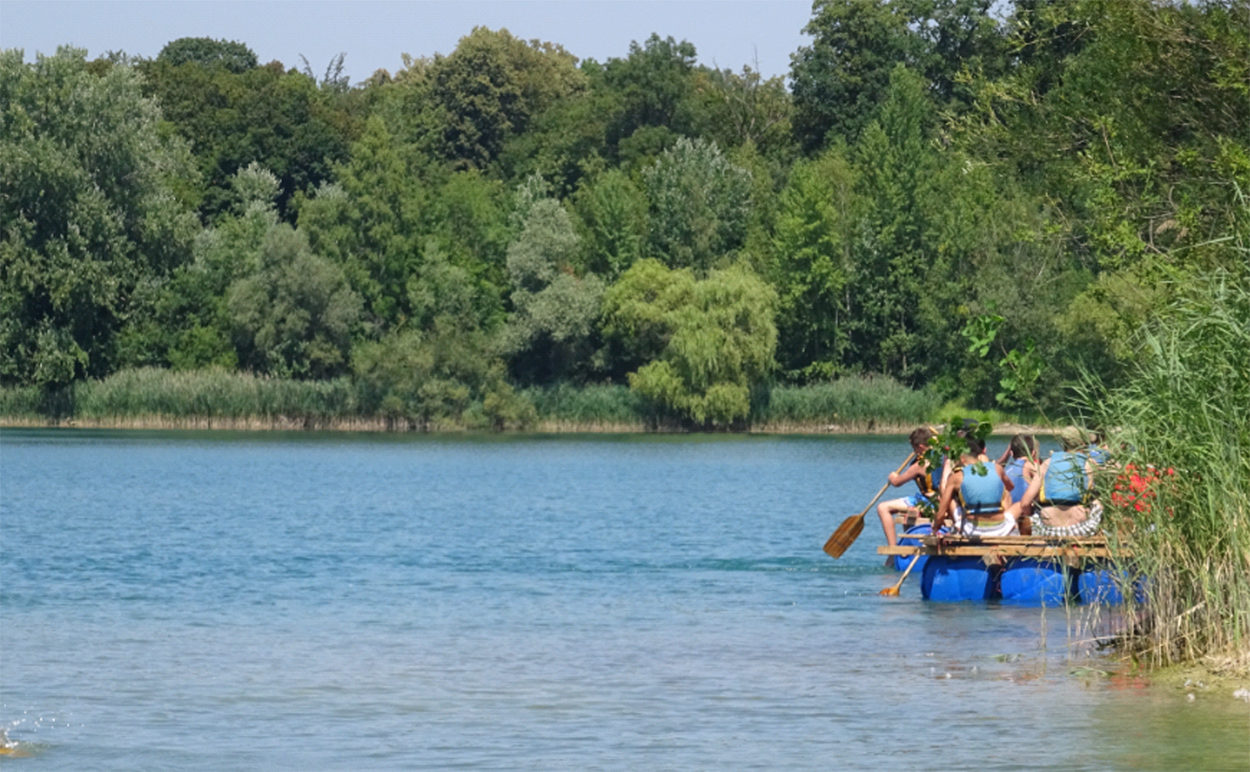 Menschen sitzen auf einem Floß und paddeln über einen blauen See.