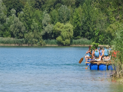 Menschen sitzen auf einem Floß und paddeln über einen blauen See.