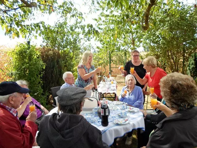 Menschen sitzen in einem Garten an einem Tisch und prosten sich zu.