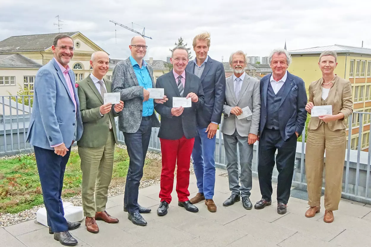 Eine Gruppe von Menschen steht auf einer Dachterrasse und hält Schecks in den Händen.