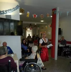 Eine blonde Frau steht in einem roten Dirndl in einem Seniorenzentrum.