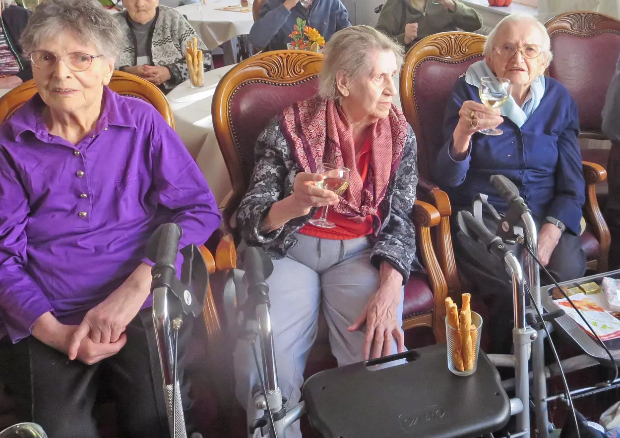 Senior*innen sitzen zusammen in Rollstühlen und trinken Wein.