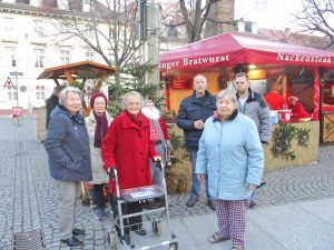 Frauen und Männer stehen vor einer Bude auf dem Weihnachtsmarkt.