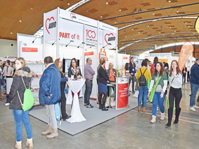 Menschen stehen an einem Stand in einer Halle.