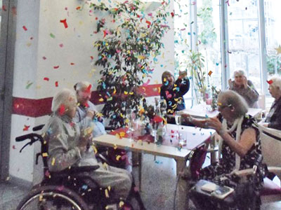 Senioren sitzen an Tischen in einem Konfetti-Regen.