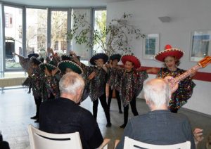 Mädchen und Jungen verkleidet mit Sombreros stehen vor Senioren und machen Musik.