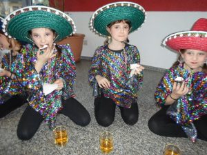 Drei Mädchen sitzen mit Sombreros auf dem Boden und essen etwas.