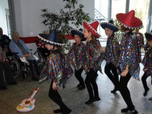 Mädchen und Jungen verkleidet mit Sombreros stehen vor Senioren und machen Musik.