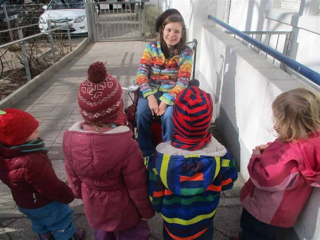 Mädchen sitzt im Rollstuhl und erzählt Kindern etwas