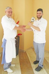 Mann übergibt einem anderem einen Kochlöffel