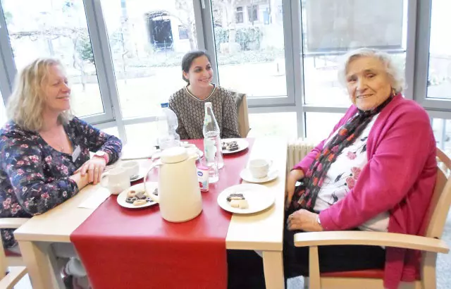 Frauen sitzen an eiFrauen und Männer sitzen an einem Tisch und schauen in die Kameranem Tisch und schauen in die Kamera