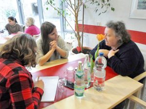 Frauen sitzen an eiFrauen und Männer sitzen an einem Tisch und schauen in die Kameranem Tisch und schauen in die Kamera