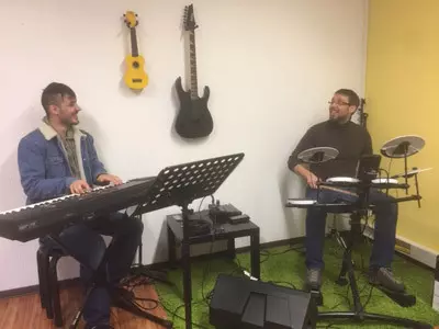 Ein Jugendicher sitzt am Keybord und ein älterer Mann daneben an einem Schlagzeug.