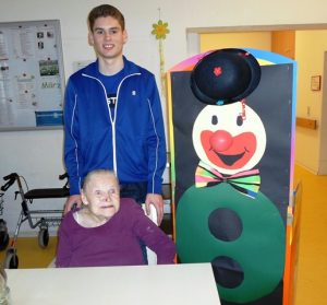 Ein junger Mann und ein Senior stehen neben einer Clownsfigur aus Pappe.