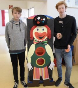 Zwei Jugendliche stehen neben einer Clownsfigur aus Pappe.