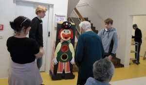 Jung und Alt stehen vor einer Clownsfigur aus Pappe.