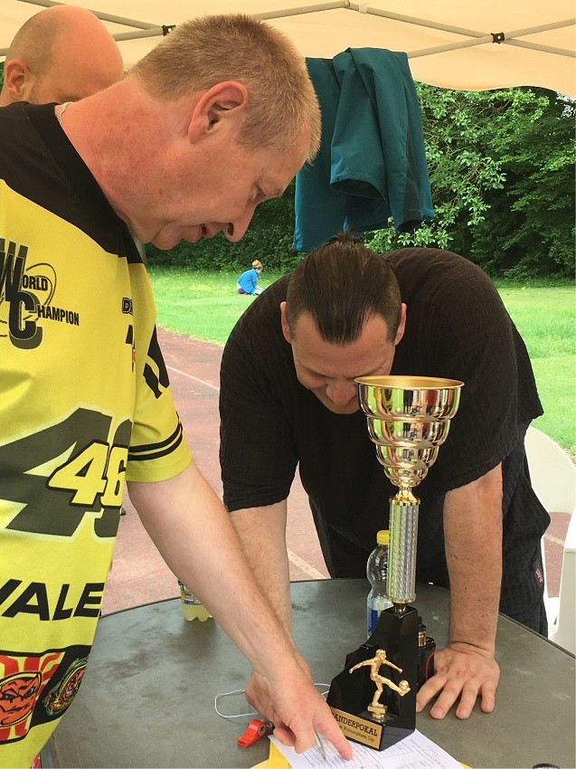 Drei Männer stehen um Pokal des Turniers und schreiben etwas